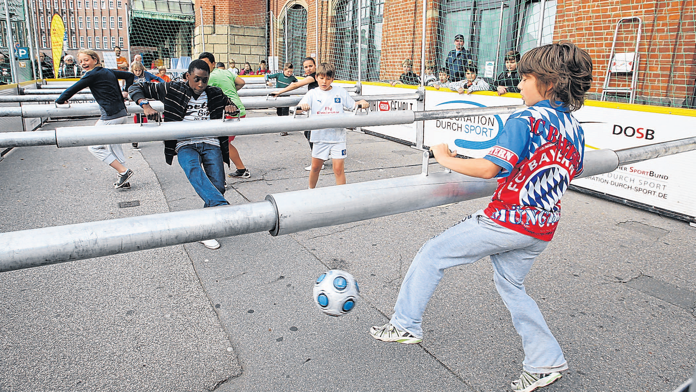 Kinder halten sich an den Haltestangen fest und versuchen den Ball zu erreichen.